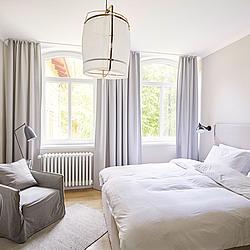 Schönes helles Zimmer mit Doppelbett, Sessel und grauen Gardinen im skandinavischen Stil.