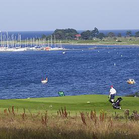 Golfer auf dem Green, im Hintergrund Segelboote auf der Förde.