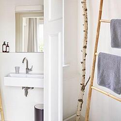 Helles Bad mit Waschbecken und Spiegel linker Hand sowie Handtuchhalter in Leiterform mit grauen Handtüchern rechts.